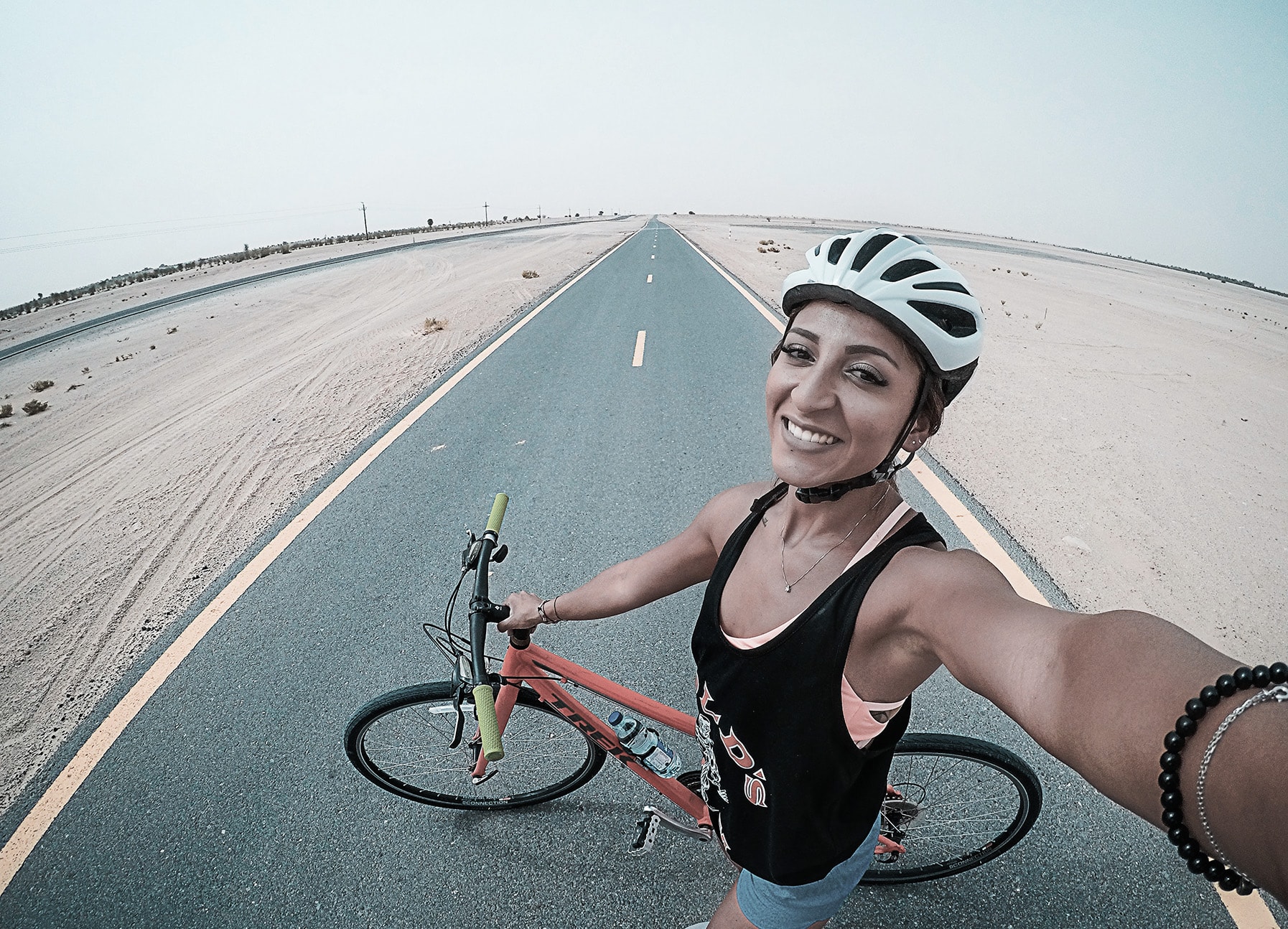 A person standing on the road with a bike taking a selfie